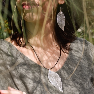 Brincos e colar prateados em forma de folha usados por mulher com camisola cinza