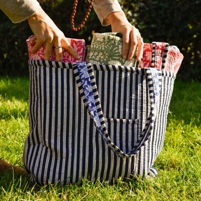 Bolsa riscas azuis e brancas com panos coloridos de padrões florais e geométricos sobre relva