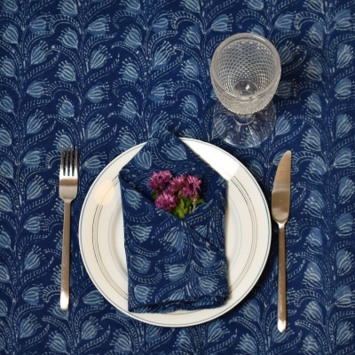 Mesa posta com prato, guardanapo azul com flores, talheres e copo de vidro