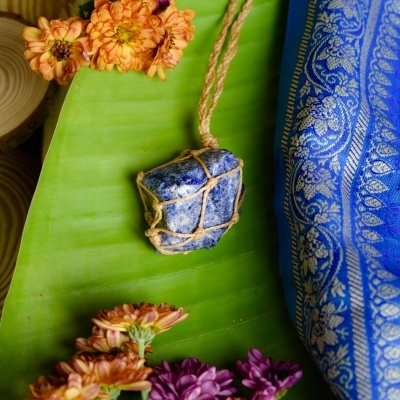 Colar com pedra azul e corda sobre folha verde com flores e tecido azul ornamental