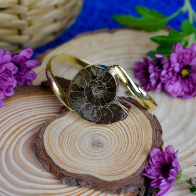 Anel dourado com pedra ammonite fosilizada sobre madeira e flores roxas