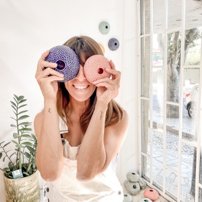 Mulher com objetos redondos coloridos perto do rosto sentada junto a janela com várias peças similares no chão
