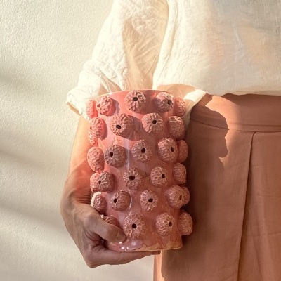 Vaso cerâmica rosa com bolhas em relevo segurado por pessoa com roupa clara.
