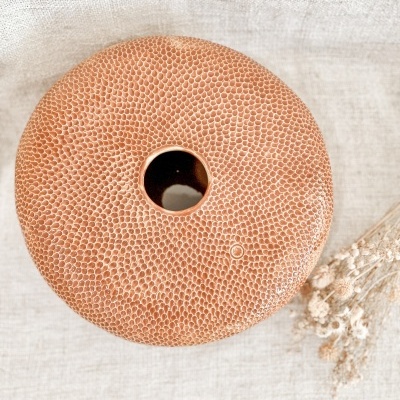 Vaso redondo castanho com textura de escamas e abertura circular no centro