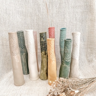 Conjunto de vasos cerâmicos altos com texturas e padrões em várias cores, sobre tecido bege, com ramos secos