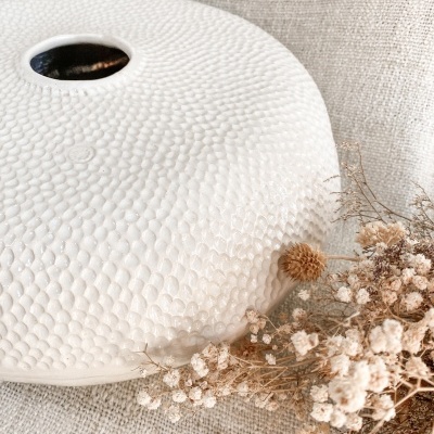 vaso branco com textura e flores secas sobre tecido bege