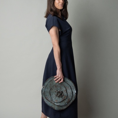 Mulher de vestido azul escuro segurando bolsa redonda texturizada azul esverdeada