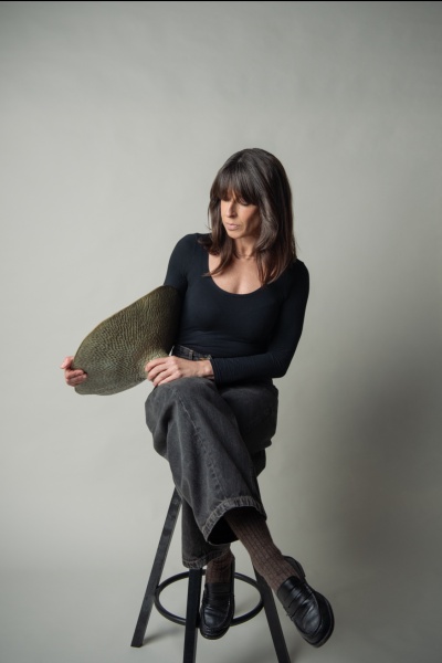 Mulher sentada num banco alto a segurar prato decorativo verde oval com padrão texturizado