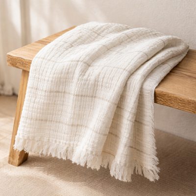 Manta creme com padrão xadrez e franjas sobre banco de madeira clara