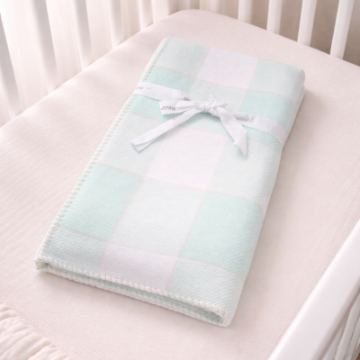 Cobertor aos quadrados azul claro e branco dobrado em berço branco.