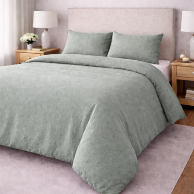 Cama com edredão e fronhas verde-acinzentadas e cabeceira estofada bege numa sala com mesas de cabeceira e candeeiros.