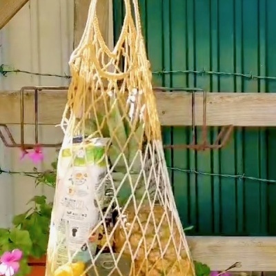 Sacola de malha bege com alimentos pendurada num varal exterior com flores