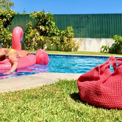 Piscina exterior com tapete insuflável rosa e bolsa vermelha na relva
