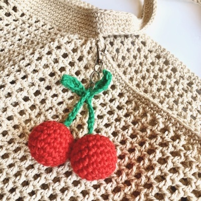 Saco de malha bege com chaveiro de cerejas vermelhas de crochê