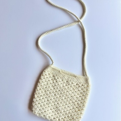 Bolsa pequena creme trançada com alça longa sobre fundo branco