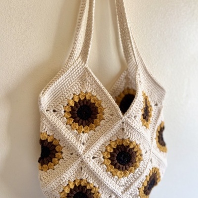 Mala de croché com padrão de quadrados coloridos pendurada numa parede branca