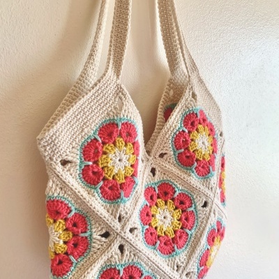 Saco de crochet creme com flores coloridas e alças largas pendurado na parede