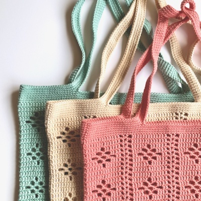 Sacos de croché em verde-água, bege e rosa com alças na mesma cor.