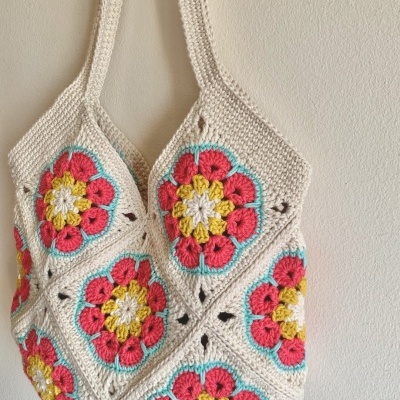 Saco de crochet com flores coloridas pendurado numa parede clara