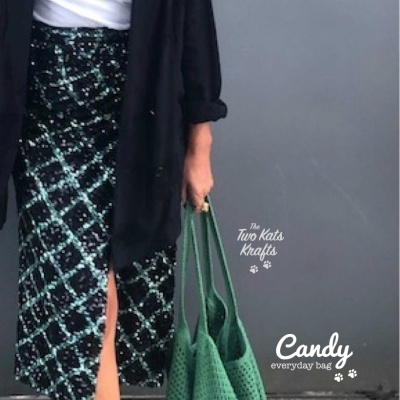 Mulher com saia xadrez, casaco preto e mala verde tricotada