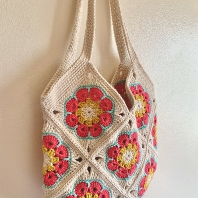 Saco crochet bege com padrões florais coloridos pendurado na parede