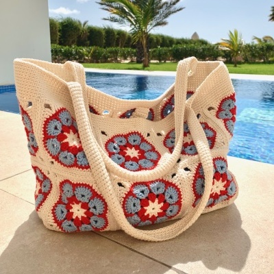 Mala de crochet creme com padrão floral vermelho e azul perto da piscina