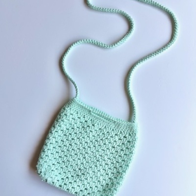 Bolsa de croché verde claro com alça longa sobre fundo branco