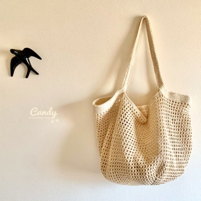 Saco de malha creme pendurado numa parede branca com decoração de pássaro preta e texto Candy