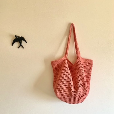 Saco de malha cor de rosa pendurado numa parede branca com uma decoração preta em forma de pássaro.