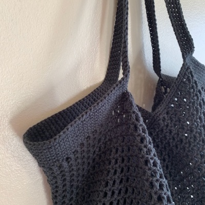 Top entrelaçado preto com alças finas pendurado numa parede branca