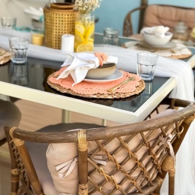 Mesa de vidro decorada com pratos cor de salmão e cadeira em rattan com almofada bege