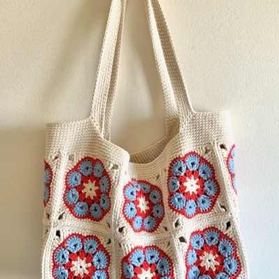 Saco de mão de crochet com padrões florais coloridos pendurado numa parede branca