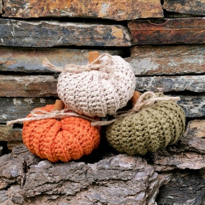 Três abóboras decorativas de croché em bege, laranja e verde com laços de corda
