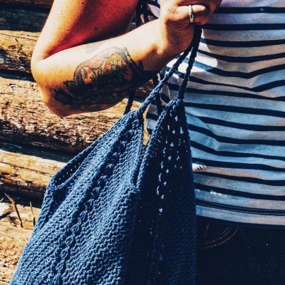 Bolsa azul escuro de malha com padrão trançado segurada por pessoa com t-shirt às riscas