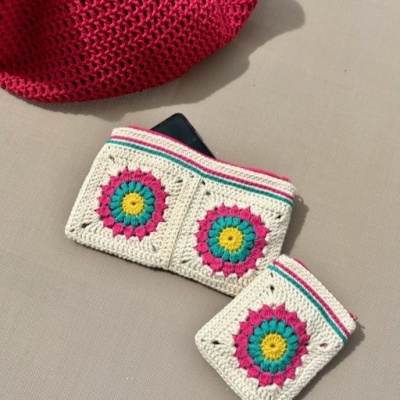 Carteira e porta-moedas de croché coloridos sobre superfície bege com chapéu vermelho.