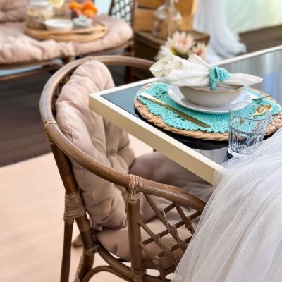 Cadeira de rattan com almofada rosa junto a mesa com louça e copo