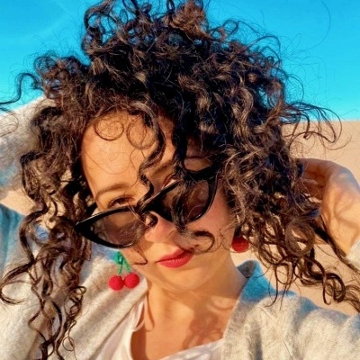 Mulher com óculos de sol, brincos de cereja e cardigan cinzento