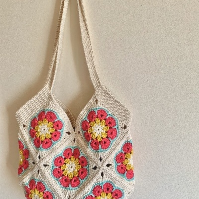 Saco de crochet com padrão colorido de flores pendurado numa parede branca