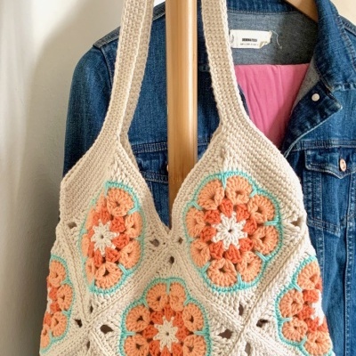 Bolsa de croché com padrão floral colorido pendurada em cabide