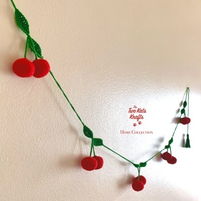 Guirlanda decorativa de croché vermelha e verde em forma de cerejas pendurada na parede.