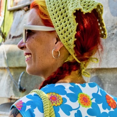 Mulher com lenço verde de crochê e blusa floral azul em ambiente urbano