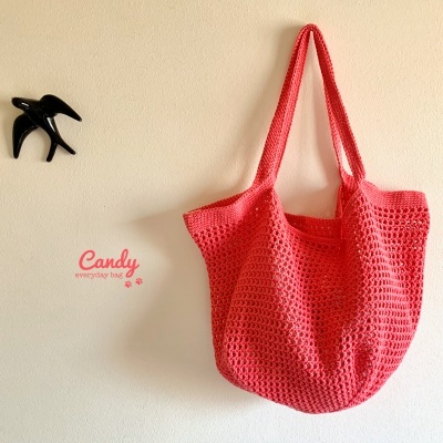 Mala de malha ou croché cor cereja pendurada numa parede clara com texto 'Candy everyday bag'