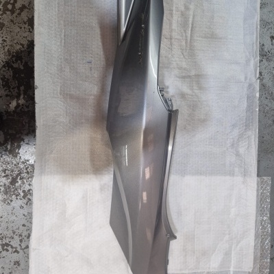 Painel lateral de motocicleta cinza metálico brilhante sobre superfície branca.