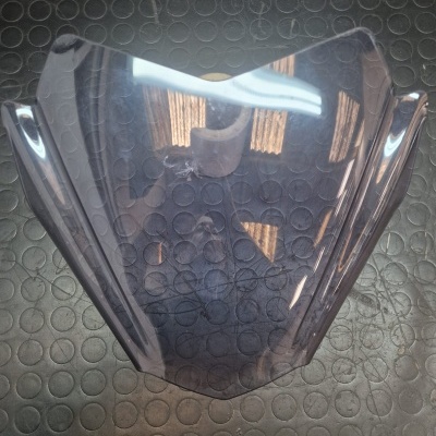 Peça de acrílico translúcido fumado para motocicleta sobre superfície preta texturizada