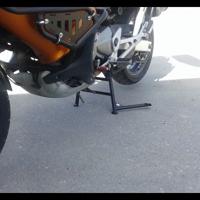 moto laranja e preta com suporte lateral e roda traseira numa superfície pavimentada