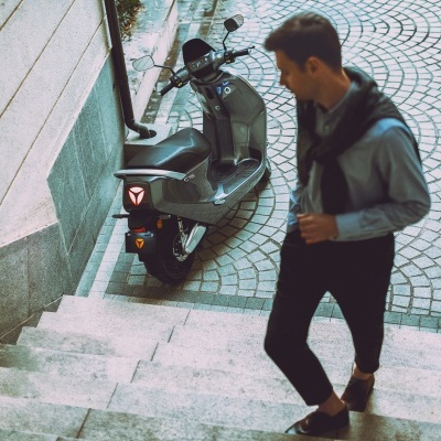 Scooter elétrica preta estacionada ao lado de escadas em calçada com homem a subir