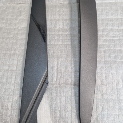 Dois painéis pretos de plástico, um brilhante e outro mate, sobre superfície clara texturada.