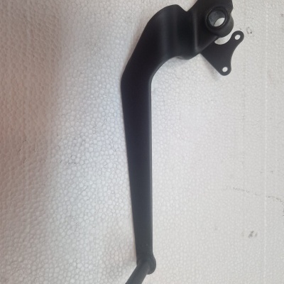 Peça metálica preta com suportes para fixação sobre superfície branca texturada