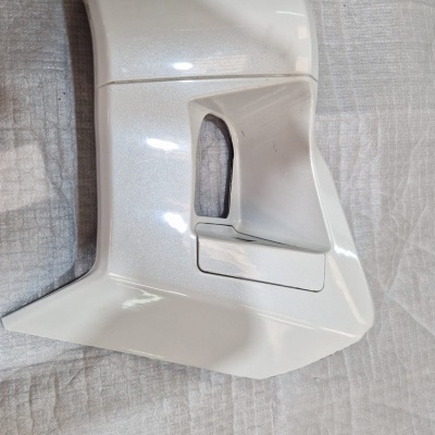 Peça automóvel branca angular sobre tecido branco com luva preta visível