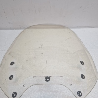 Para-brisas transparente curvo com fixadores pretos sobre superfície branca.